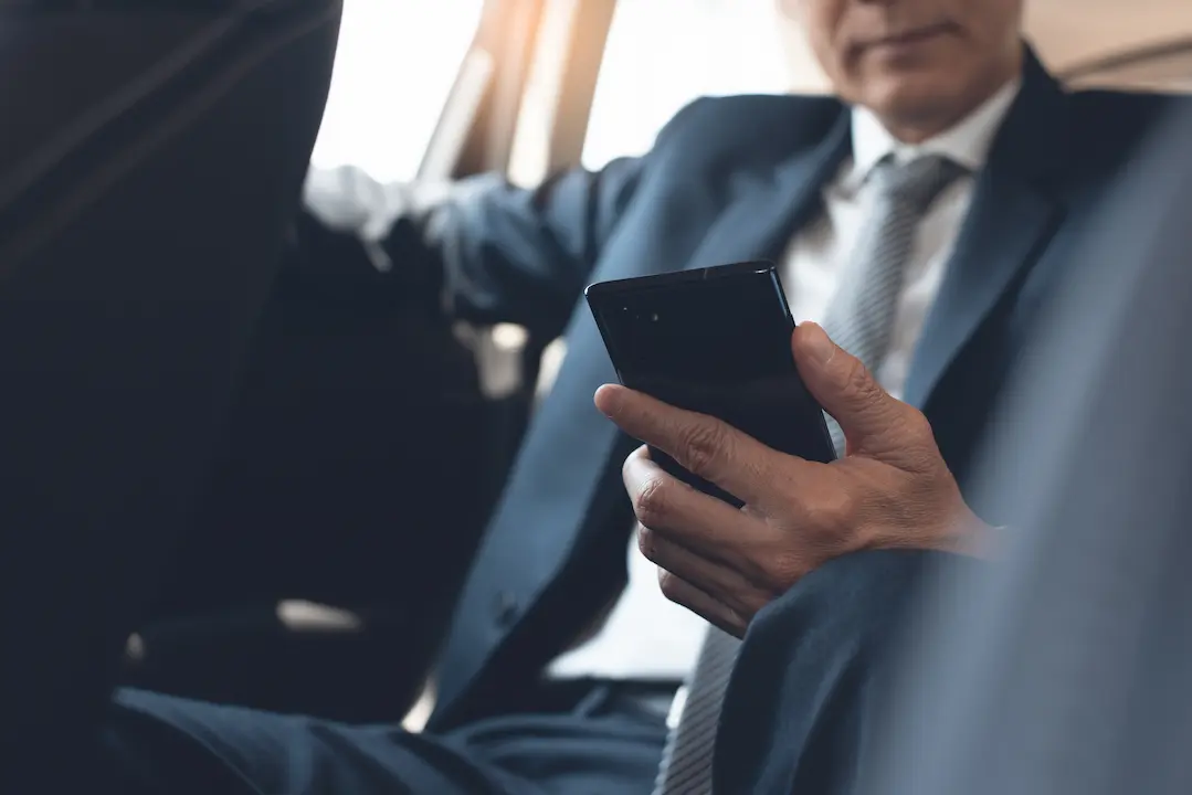 photo of man wearing a suit in back seat of car answering phone. the top of is face is cropped out of the image.